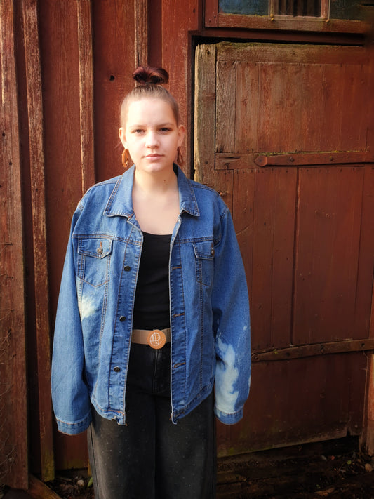 Front view of “The King of the Clouds” hand-painted and bleached upcycled denim jacket, modeled outdoors.