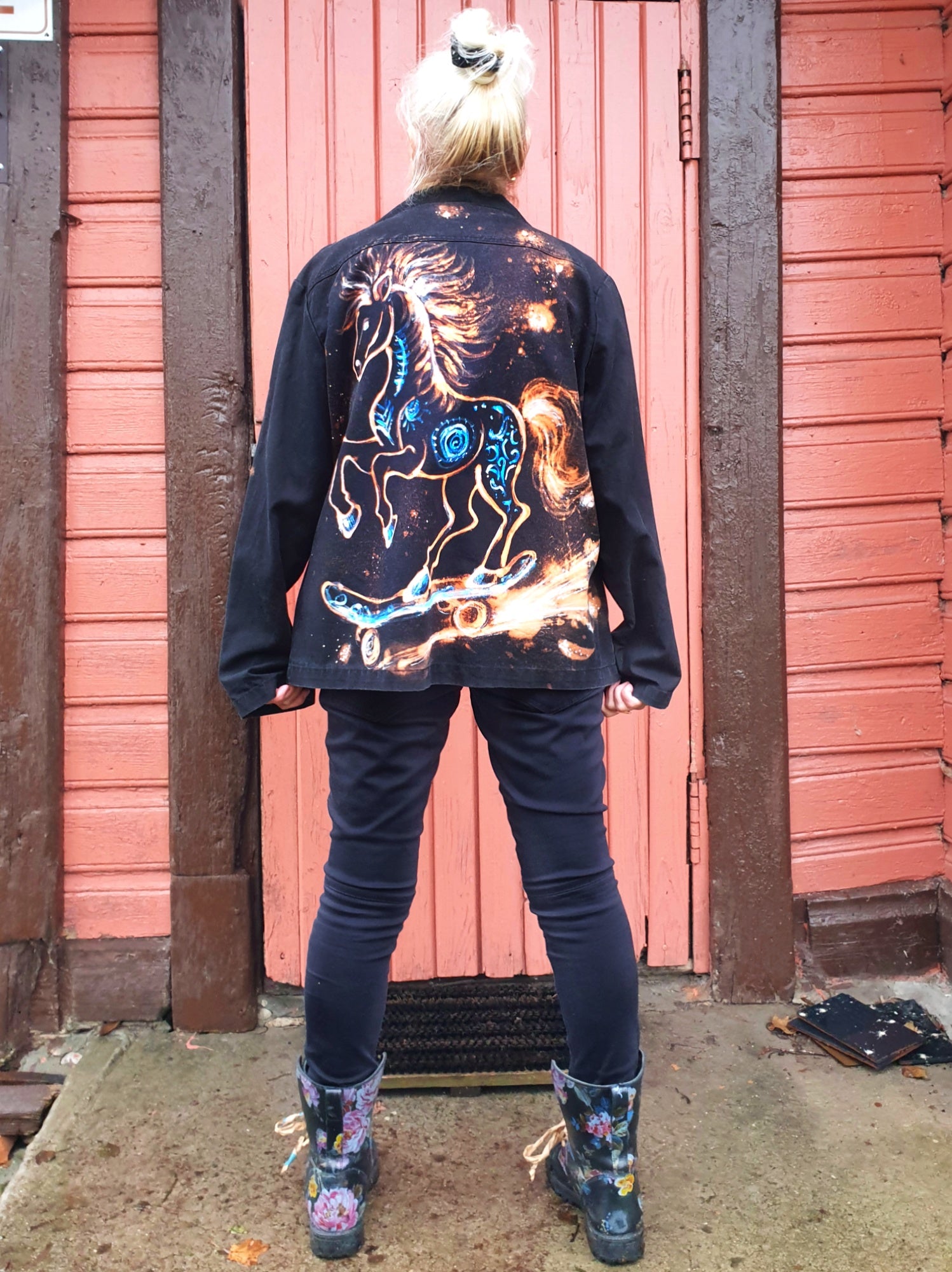 Back view of the “Cosmic Skatehorse” hand-painted black cotton jacket featuring a horse on a skateboard painted in white and blue.