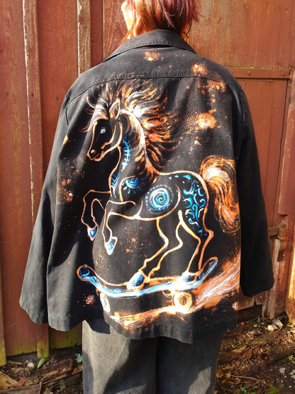 Back view of the “Cosmic Skatehorse” hand-painted black cotton jacket featuring a horse on a skateboard painted in white and blue.