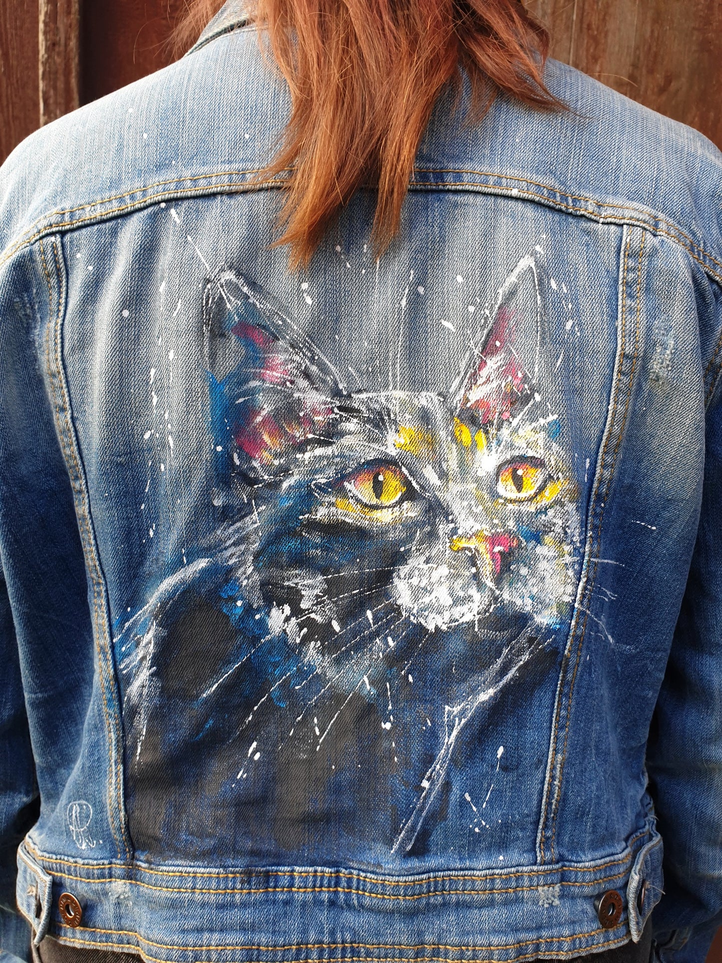 Back view of the “Midnight Whiskers” hand-painted denim jacket featuring a black cat with glowing yellow eyes.