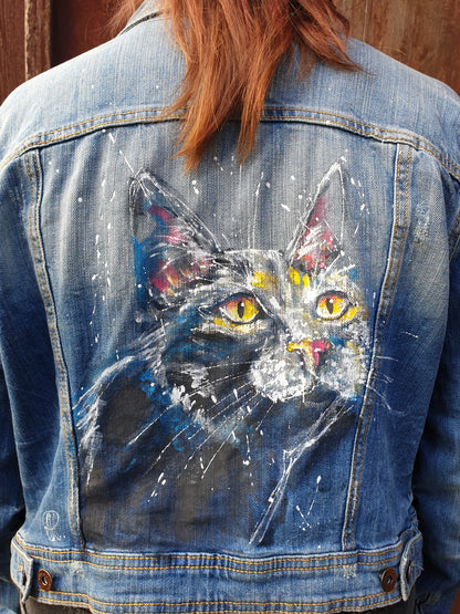 Back view of the “Midnight Whiskers” hand-painted denim jacket featuring a black cat with glowing yellow eyes.