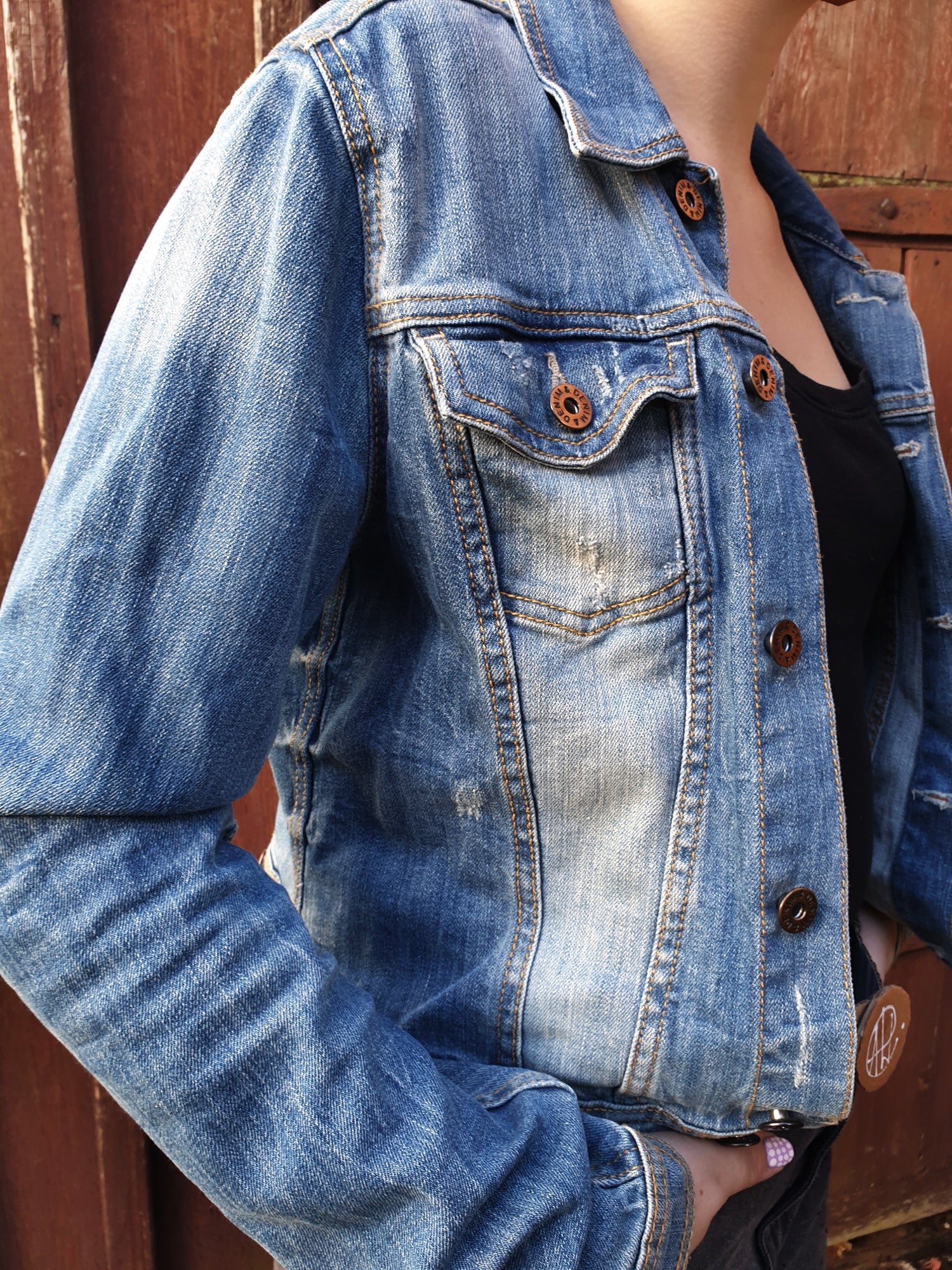 Front view of the slightly distressed upcycled denim jacket with two chest pockets and button closure.