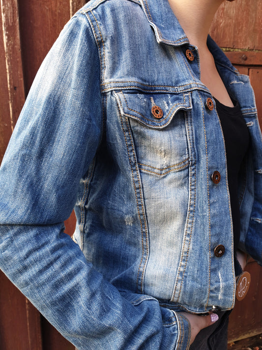 Front view of the slightly distressed upcycled denim jacket with two chest pockets and button closure.