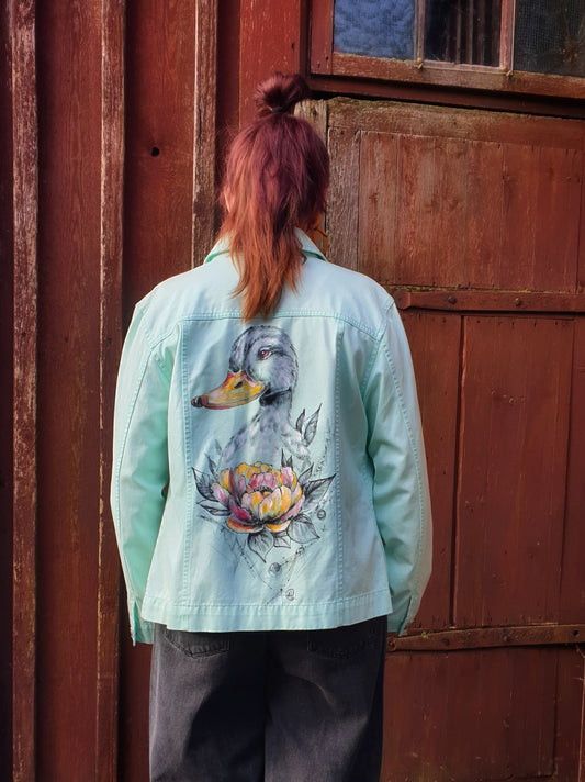 Back view of the “Pretty Fancy Duck” hand-painted mint-green denim jacket featuring a duck and a colorful flower.