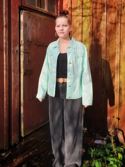 Front view of the light green upcycled denim jacket with two pockets and button closure.