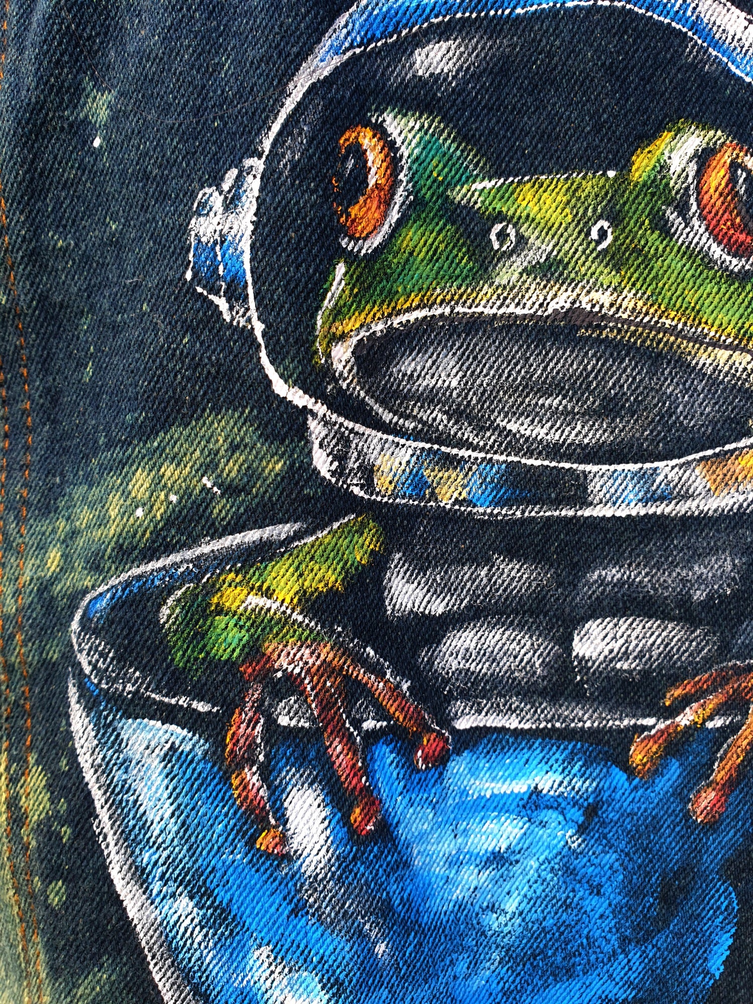 Close-up of colorful frog astronaut painted on denim – original wearable art by Hele Artwear.