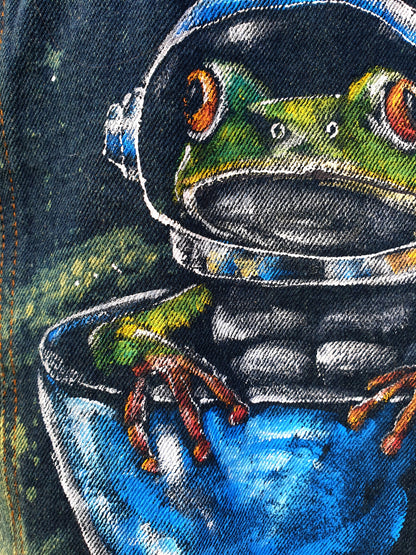 Close-up of colorful frog astronaut painted on denim – original wearable art by Hele Artwear.